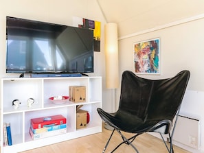 A modern living room with a flat-screen TV on a white shelf, a black leather chair, and a colorful abstract painting on the wall. - 4 Person Holiday Home in Gedser (Gedser)