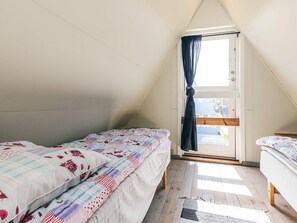 A small, triangular attic bedroom with two beds, a wooden floor, and a window with curtains.
