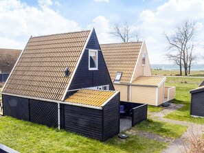 A row of modern, dark-colored cabins with sloped roofs, arranged in a grassy area with a view of the sea.
