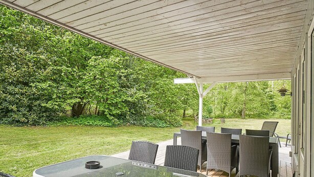 Un área de patio al aire libre con mesa y sillas, rodeada por una terraza de madera y una sección cubierta con techo blanco.