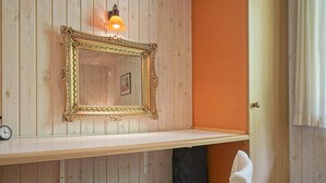 Una habitación con un panel de madera, un espejo con marco decorativo, un reloj pequeño y una silla blanca.