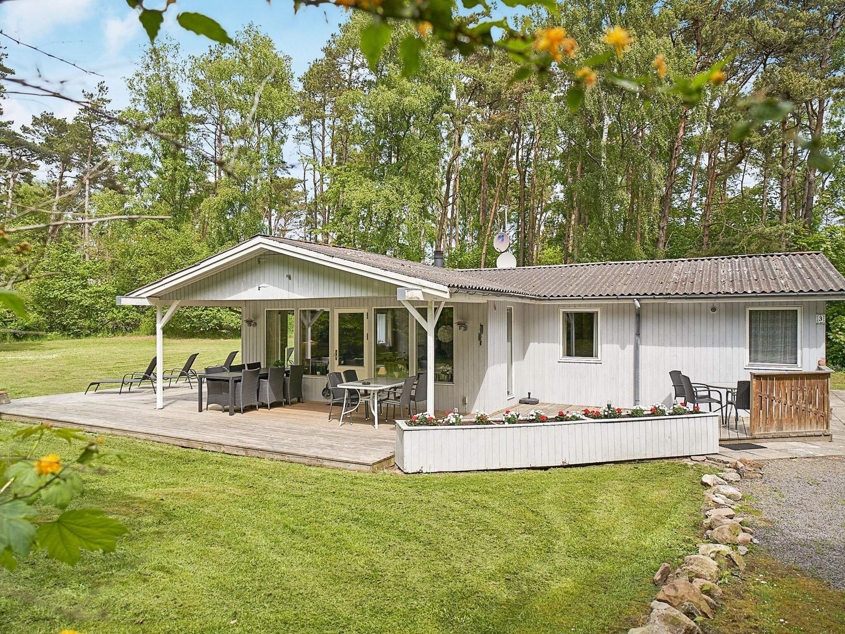 Uma cabana térrea com varanda coberta, área de estar externa e um pequeno jardim.