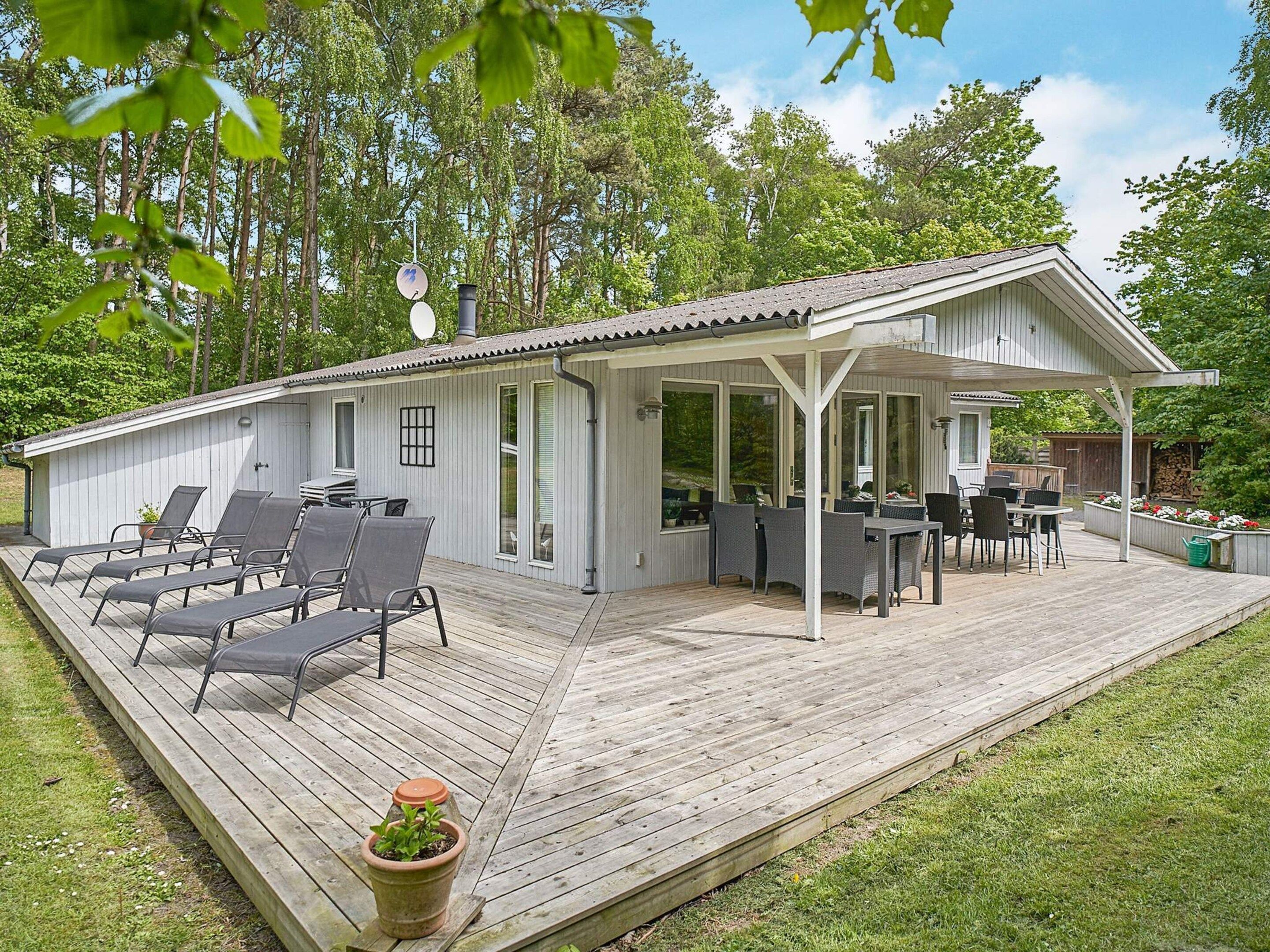 Een overdekt terras buiten met zitplaatsen en een eethoek, omgeven door bomen.