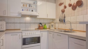 Una cocina con alacenas blancas, estufa, lavavajillas y varios utensilios de cocina en la pared.