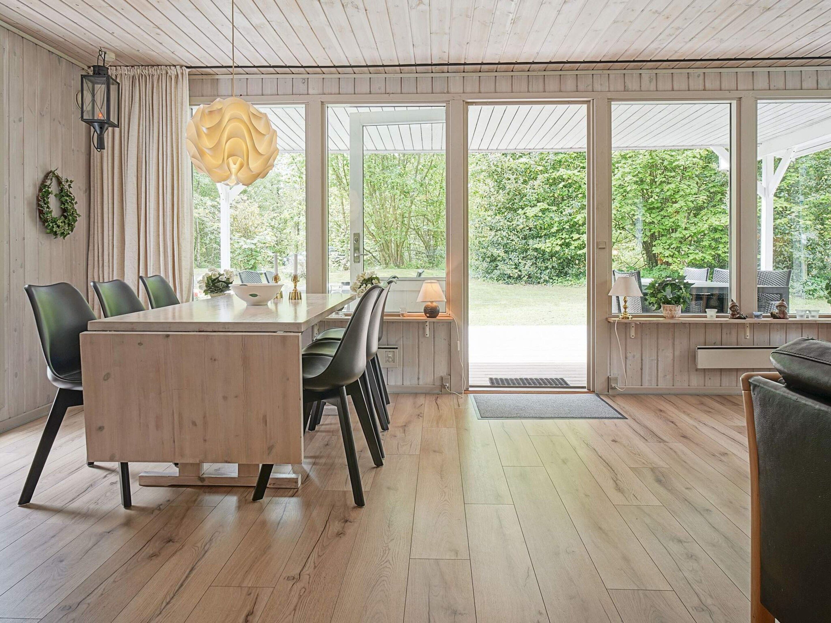 A spacious dining area with a wooden table and chairs, large windows, and a view of greenery outside.