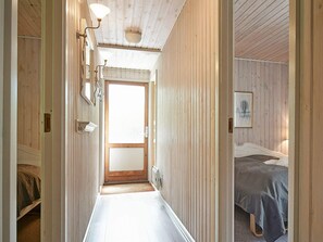 Um corredor estreito com paredes de madeira e uma porta que dá para um quarto, com uma cama e um quadro na parede.