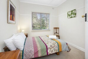 A bedroom with a bed, a window with blinds, a chair, and a door. - Allambee Cottage - pet friendly, close to town & the station (Katoomba)