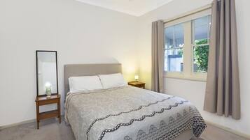A bedroom with a bed, a nightstand, a mirror, and a window with curtains.