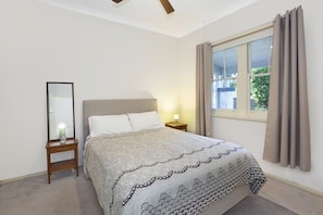 A bedroom with a bed, a nightstand, a mirror, and a window with curtains. - Allambee Cottage - pet friendly, close to town & the station (Katoomba)