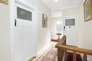 A hallway with white walls, a wooden handrail, and a patterned carpet. - Allambee Cottage - pet friendly, close to town & the station (Katoomba)
