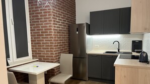 A compact kitchen with a brick wall, a stainless steel refrigerator, a sink, and a kettle. - Tony's Apartments (Rijeka)