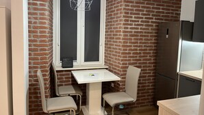 A small kitchen with a white table and two chairs, a hanging light fixture, and a brick wall. - Tony's Apartments (Rijeka)