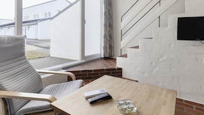 Een moderne woonkamer met een groot raam, een bank, een tafel en een trap.