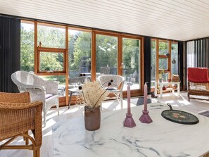 A room with large windows, wicker furniture, a marble table, and a vase with dried flowers.