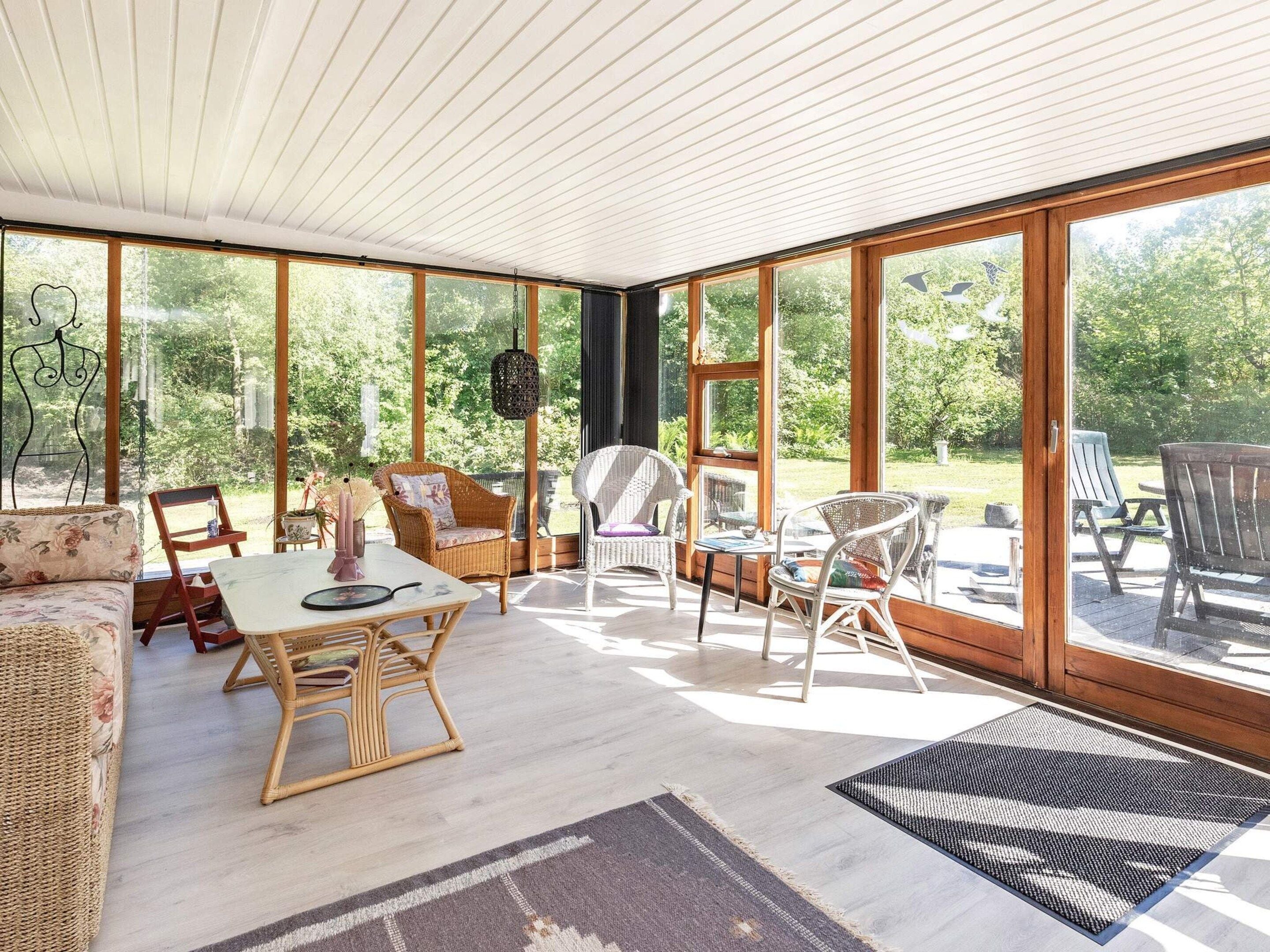 Una habitación amplia con ventanas grandes, muebles de mimbre y techo de madera.