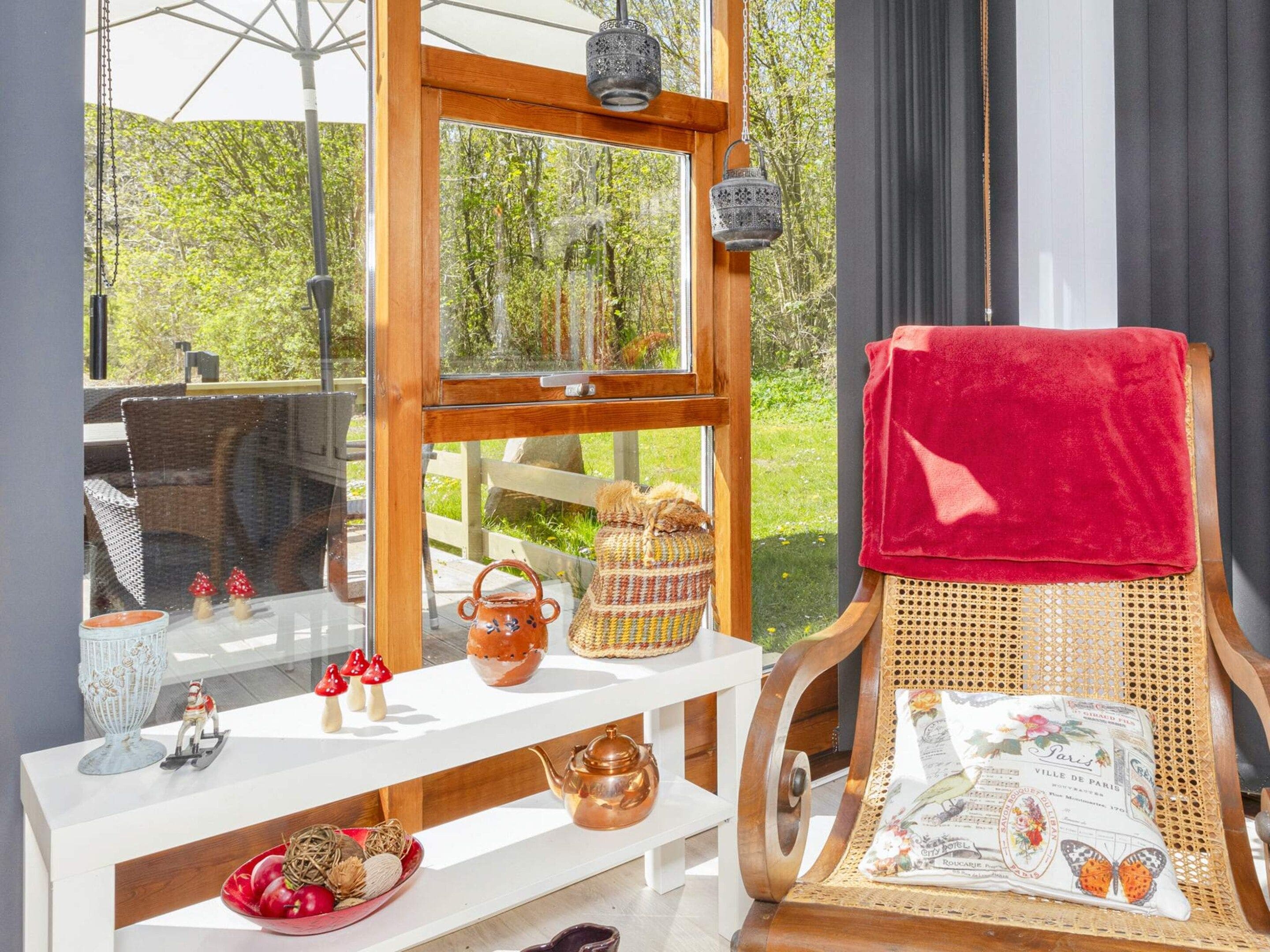 A room with a wooden chair, a white shelf with decorative items, and a window with a view of greenery.