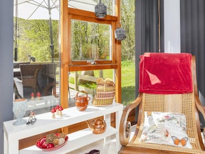A room with a wooden chair, a white shelf with decorative items, and a window with a view of greenery.