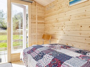 A wooden cabin bedroom with a large bed, a chair, and a view of a grassy area through a glass door.