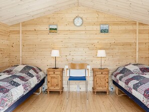A cozy room with two beds, wooden walls, a clock, and framed pictures.