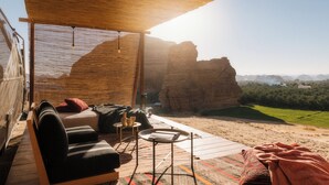 A cozy outdoor seating area with a sofa, a small table, and a blanket, overlooking a scenic canyon view. - Caravan by Habitas (Al-'Ula)
