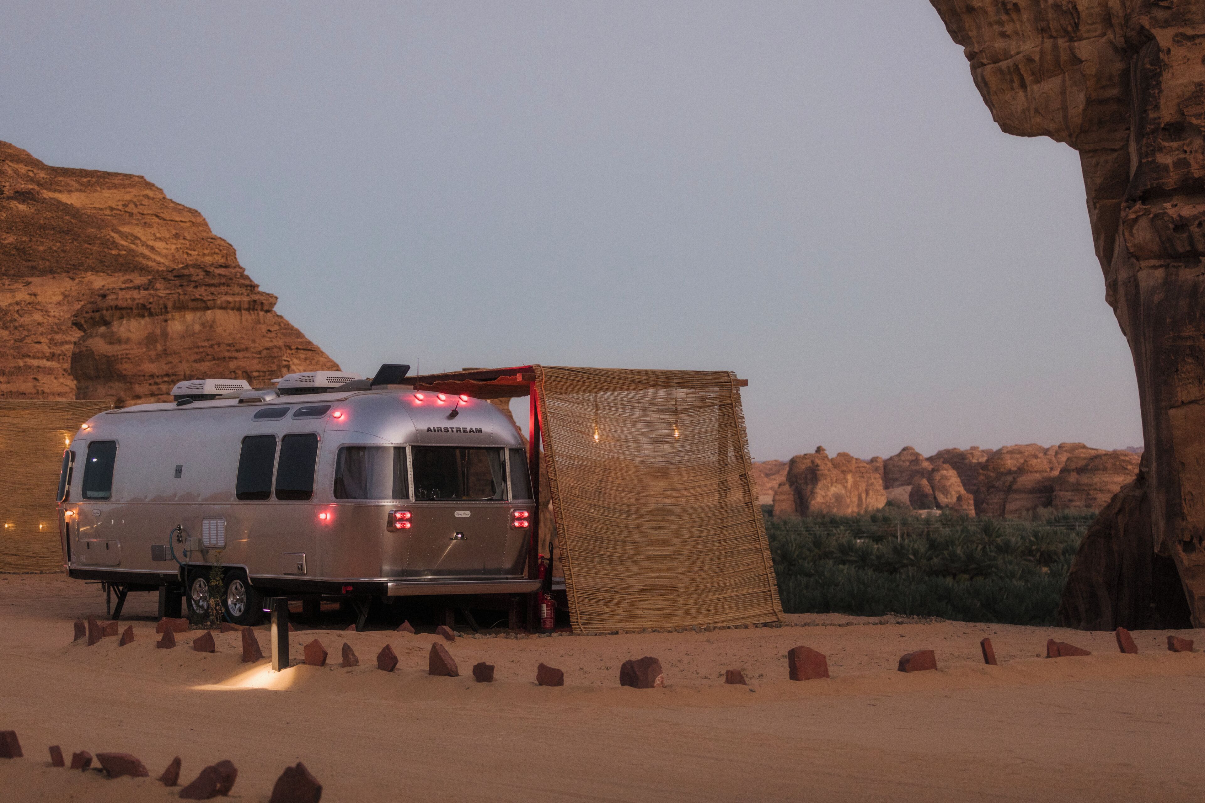 A silver RV parked in a desert with rocky cliffs in the background.