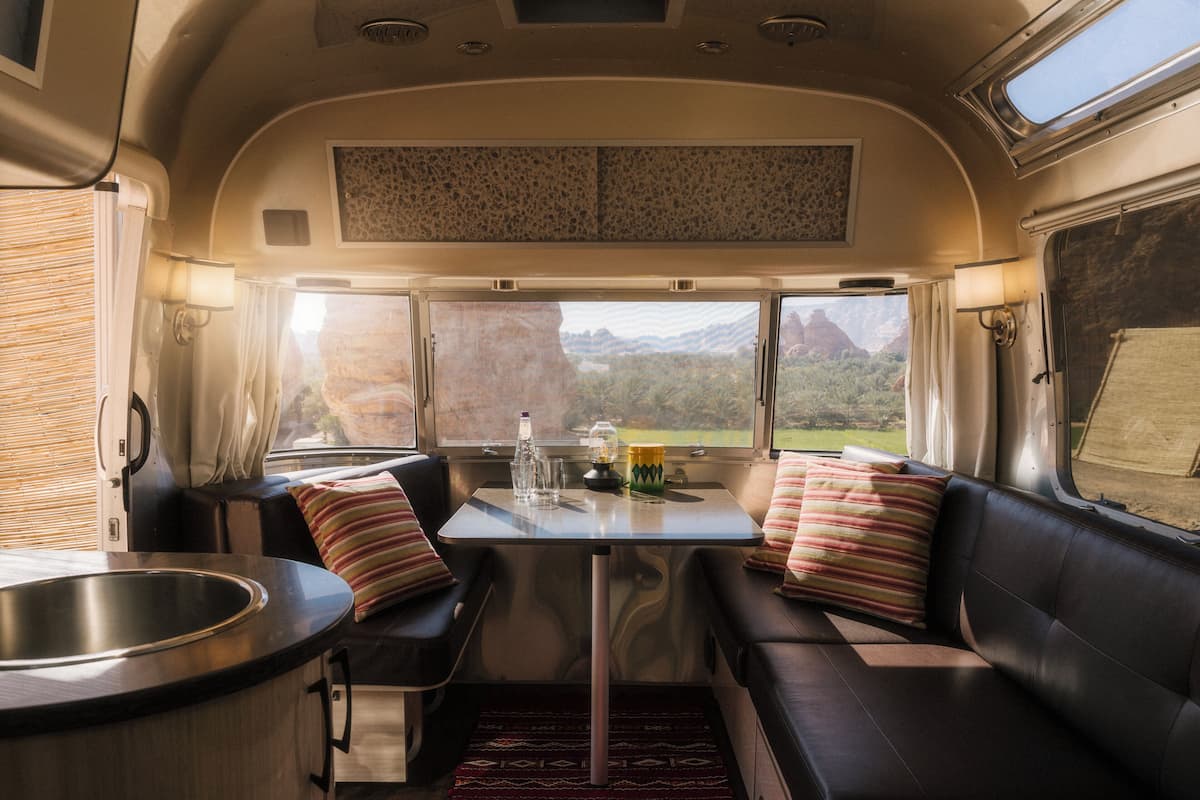 A compact RV interior with a kitchenette, seating area, and a table with a view of the outdoors.