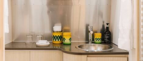 Una cocina compacta con un lavamanos, dos frascos amarillos con diseños verdes, un dispensador de jabón y una toalla blanca colgada en la pared.
