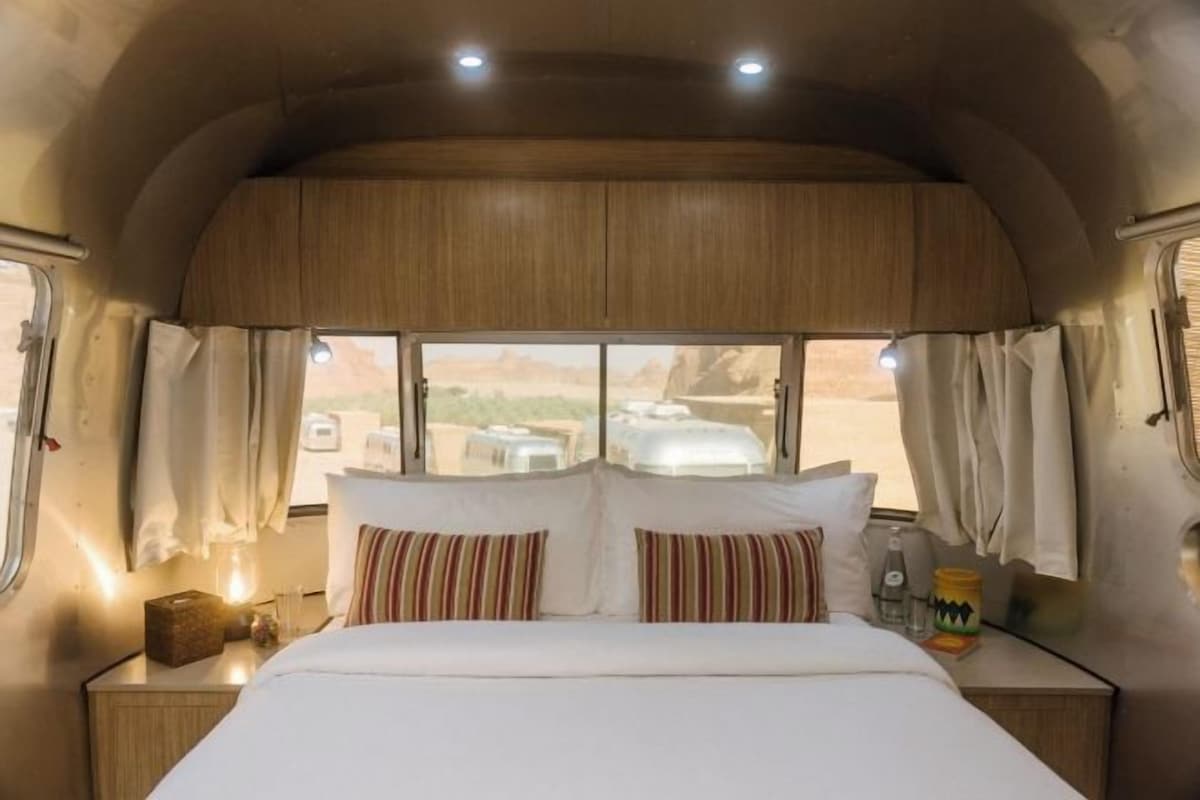 A cozy RV bedroom with a bed, curtains, and a window offering a desert view.