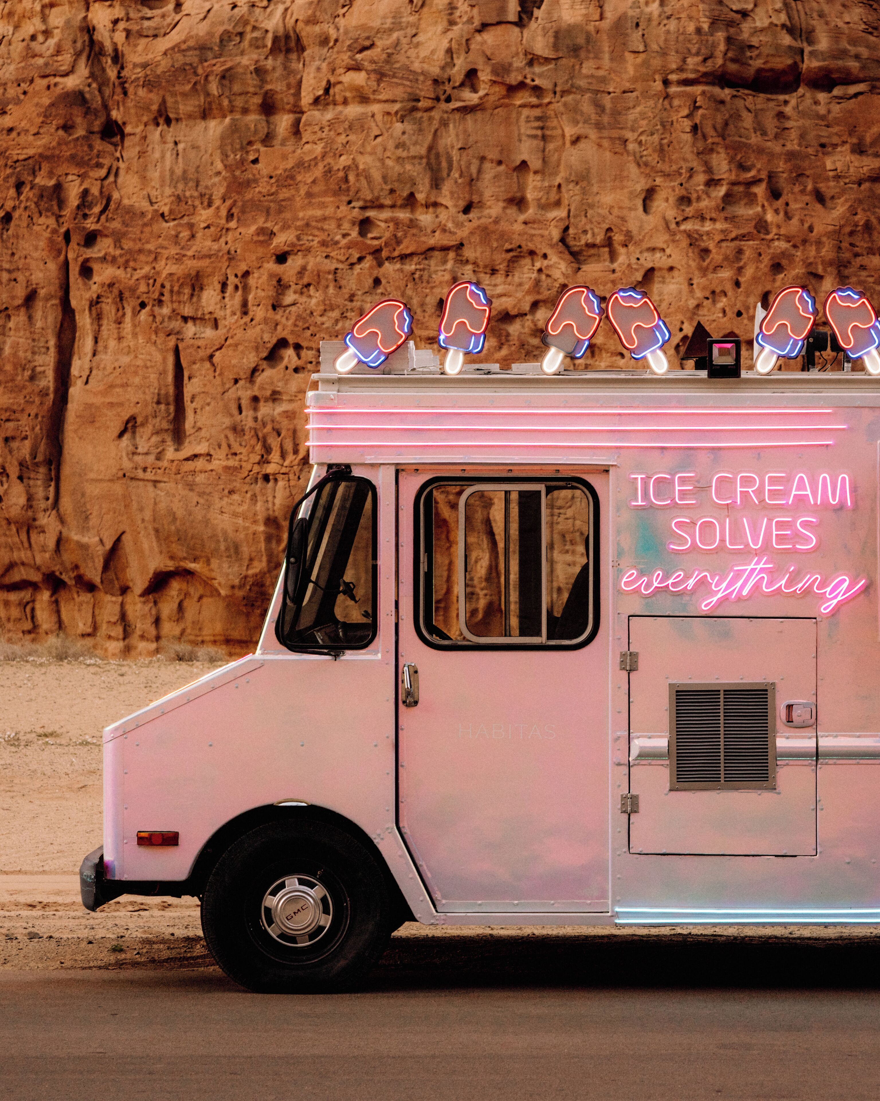 A pink ice cream truck parked in front of a rocky background.