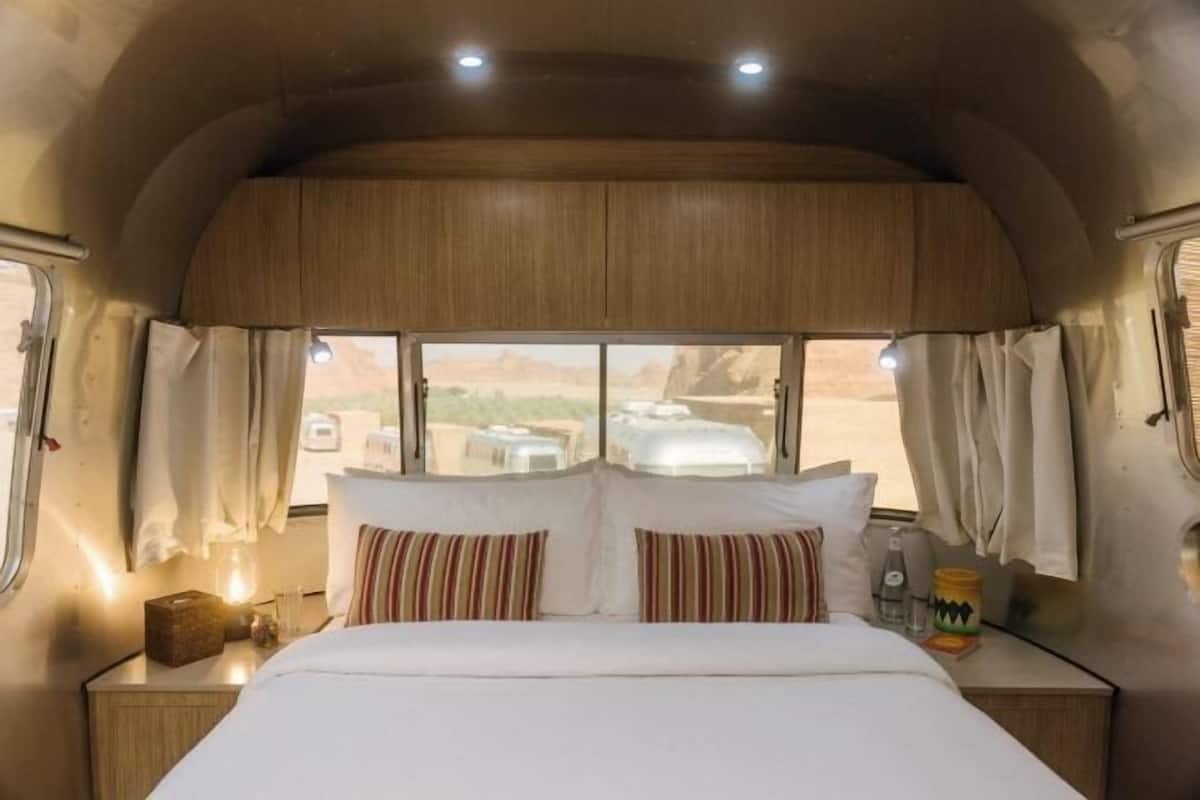 A cozy RV bedroom with a bed, curtains, and a window offering a desert view.