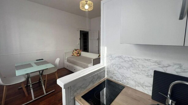 Une cuisine compacte dotée d’une cuisinière intégrée, un coin repas avec une table et des chaises, et un petit espace détente avec un banc.