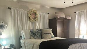 Ein Schlafzimmer mit einem Bett, einem Nachttisch, einer Kommode, einem Deckenventilator und einem Fenster mit Vorhängen.