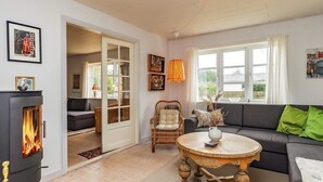 A cozy living room with a fireplace, a sofa, a round wooden table, and a wicker chair. - 5 Person Holiday Home in Laeso (Læsø)