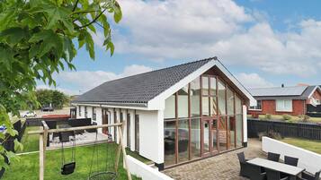 Una casa moderna con un amplio ventanal, un patio con mobiliario exterior y un columpio.