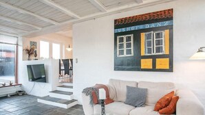 Un salon avec un canapé, une table basse en verre et un tableau représentant un bâtiment accroché au mur.