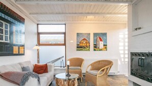 Un salon avec un canapé blanc, deux fauteuils en osier, une table basse en verre et des œuvres d’art accrochées au mur.