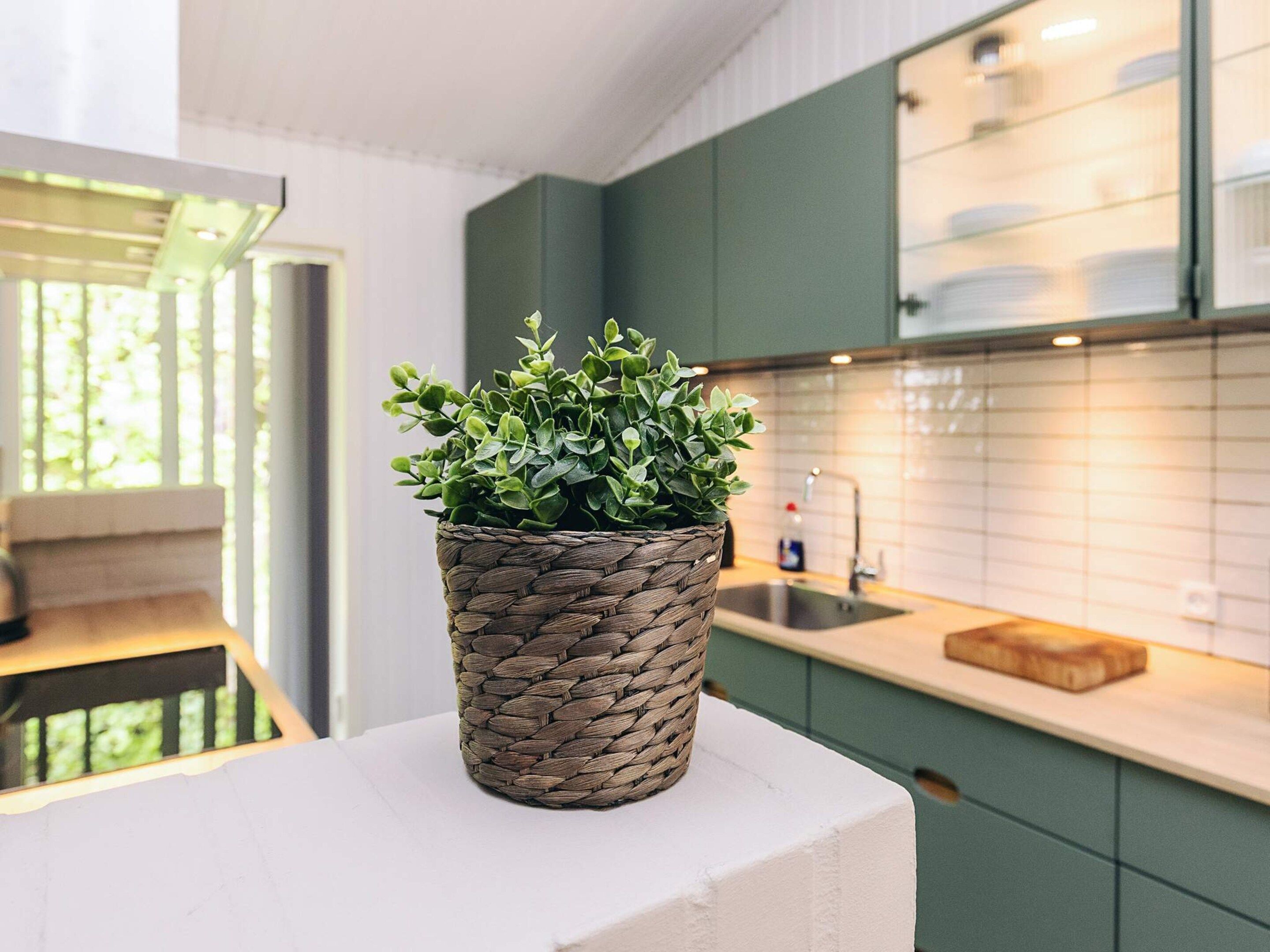 Et moderne køkken med grønne skabe, en hvid bordplade og en flettet kurv med en grøn plante.