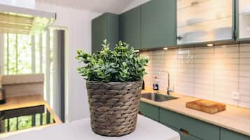Et moderne køkken med grønne skabe, en hvid bordplade og en flettet kurv med en grøn plante.