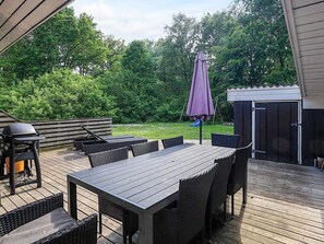 An outdoor patio with a wooden table and chairs, a grill, and a covered umbrella.