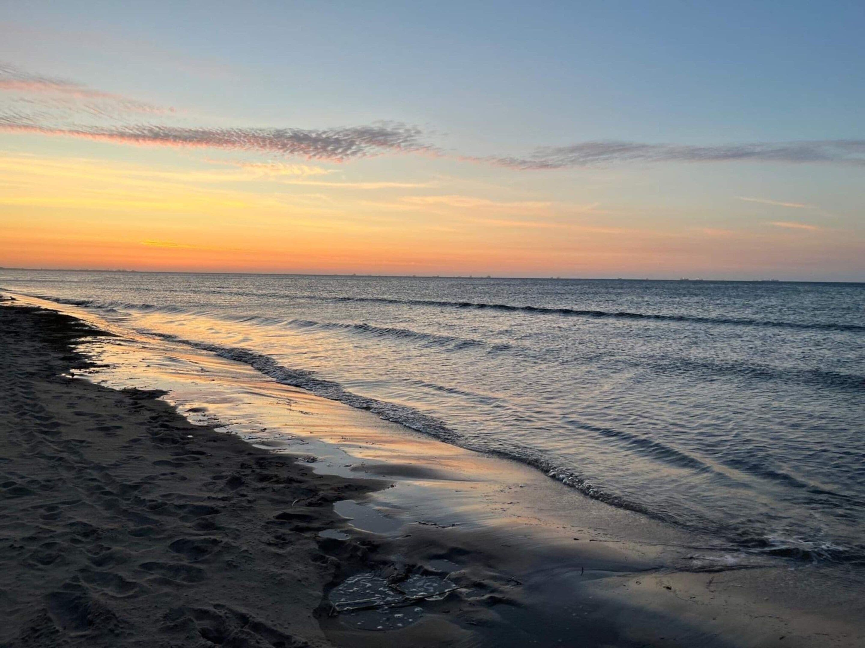 Une plage avec des vagues, un ciel dégagé et un coucher de soleil.