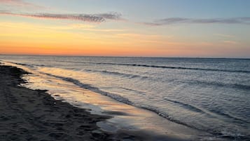 En strand med bølger, klar himmel og solnedgang.