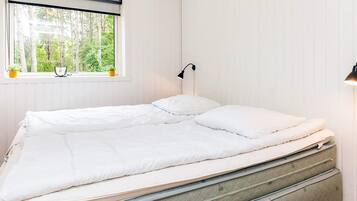 Et enkeltværelse med et vindue, en sengebordlampe og udsigt til træer.