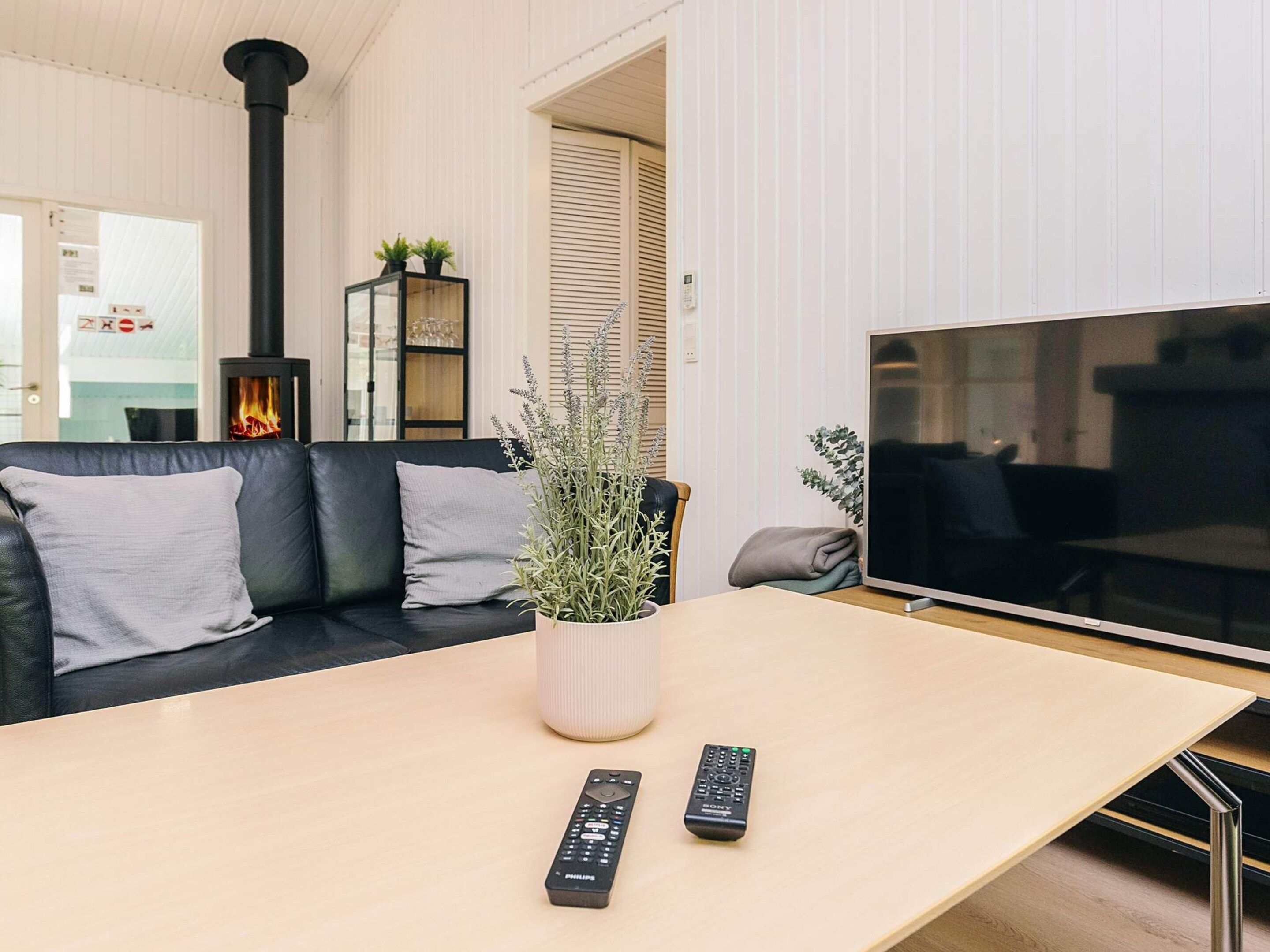 En moderne stue med en sort lædersofa, et træ sofabord, et stort fladskærms TV og en pejs.