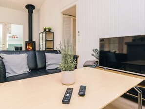 A modern living room with a black leather sofa, a wooden coffee table, a large flat-screen TV, and a fireplace.