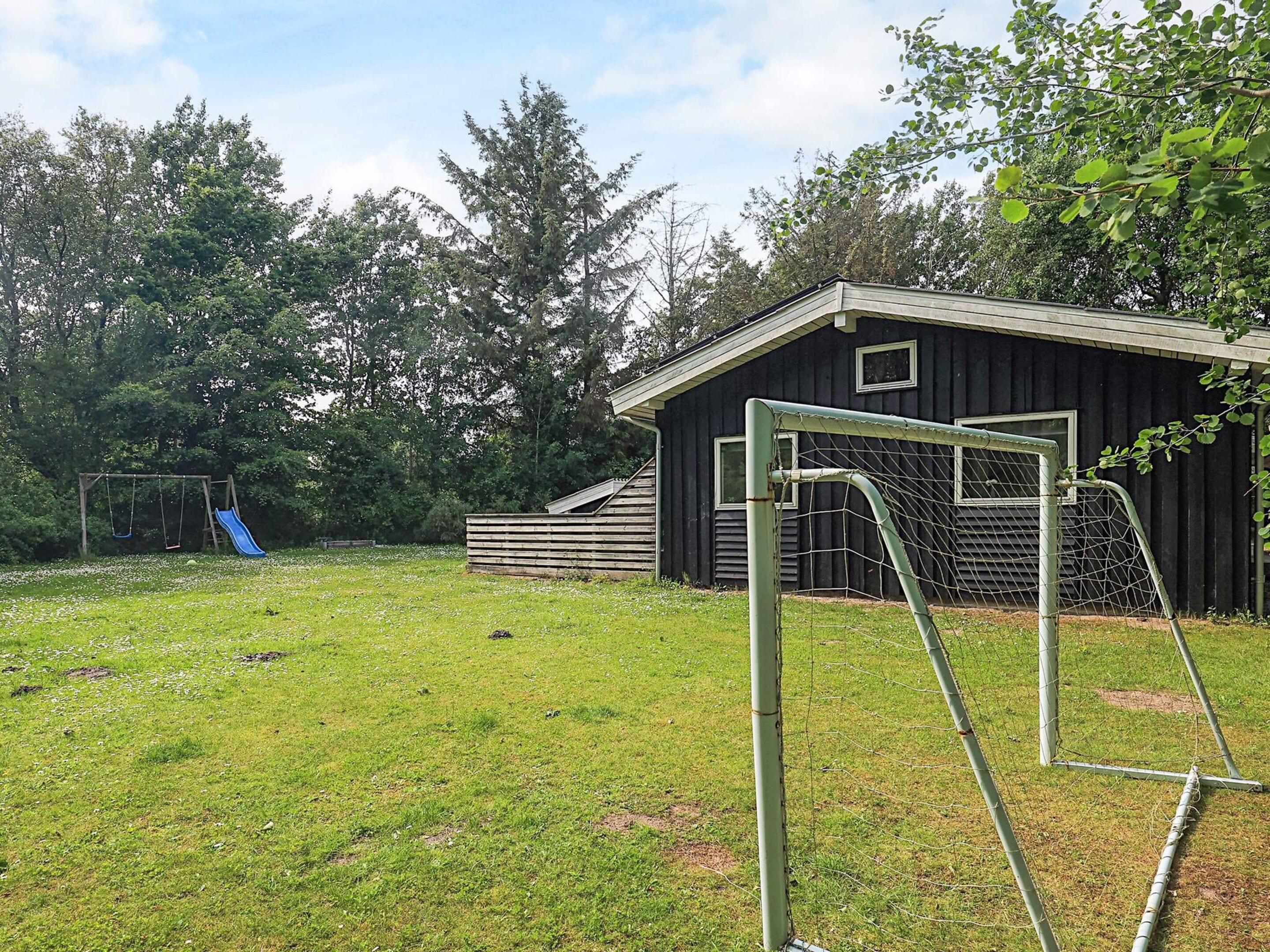 A grassy outdoor area with a swing set, a blue slide, and a fenced soccer goal.