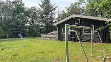 En græsplæne med gyngestativ, blå rutsjebane og et hegn om fodboldmålet.