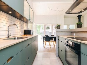 A modern kitchen with a central island, a dining area with a table and chairs, and a view of the outdoors.