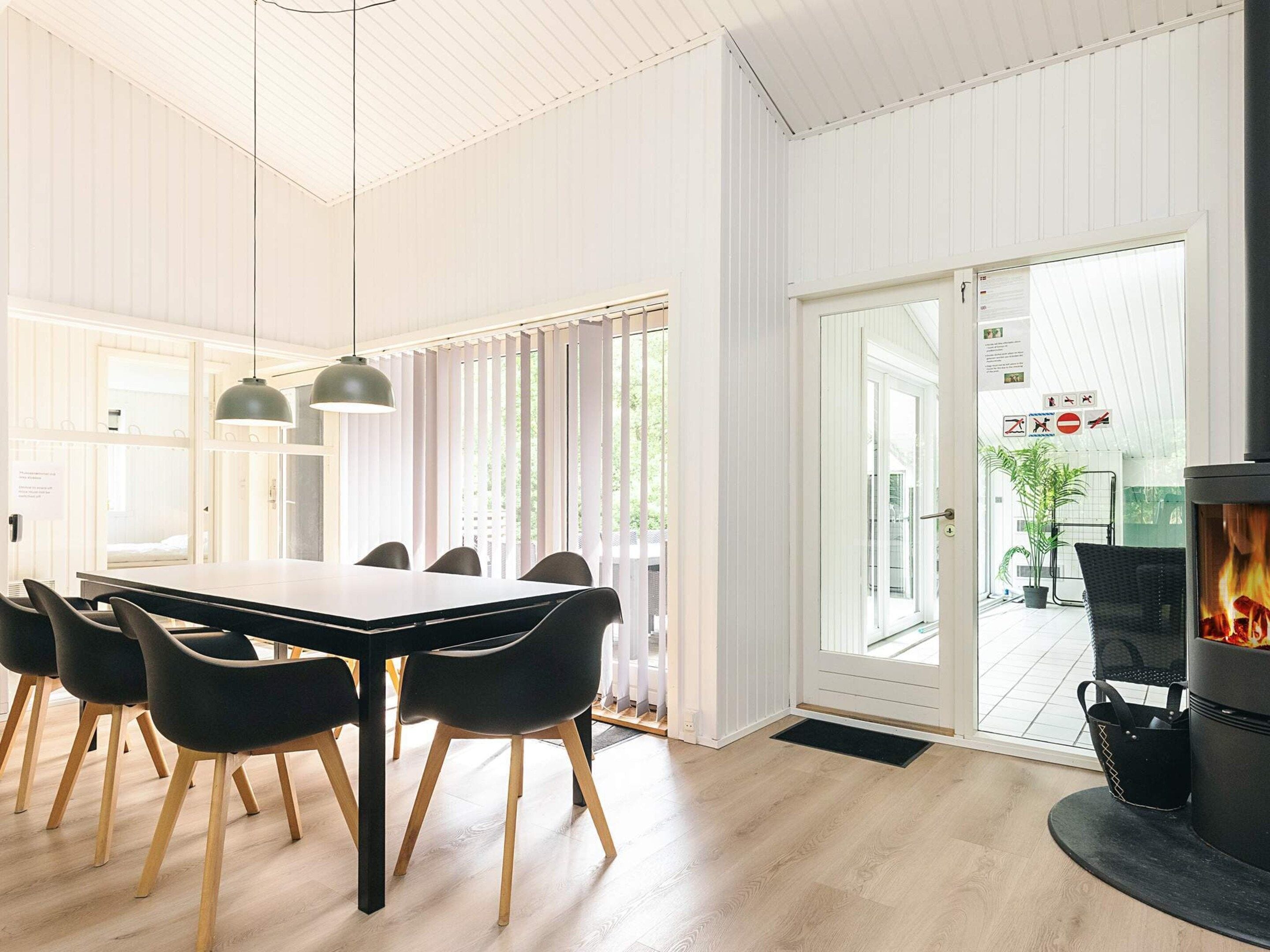Et moderne spiseområde med et langt bord og sorte stole, en pejs og udsigt over naturen gennem store glasdøre.