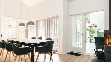 Et moderne spiseområde med et langt bord og sorte stole, en pejs og udsigt over naturen gennem store glasdøre.