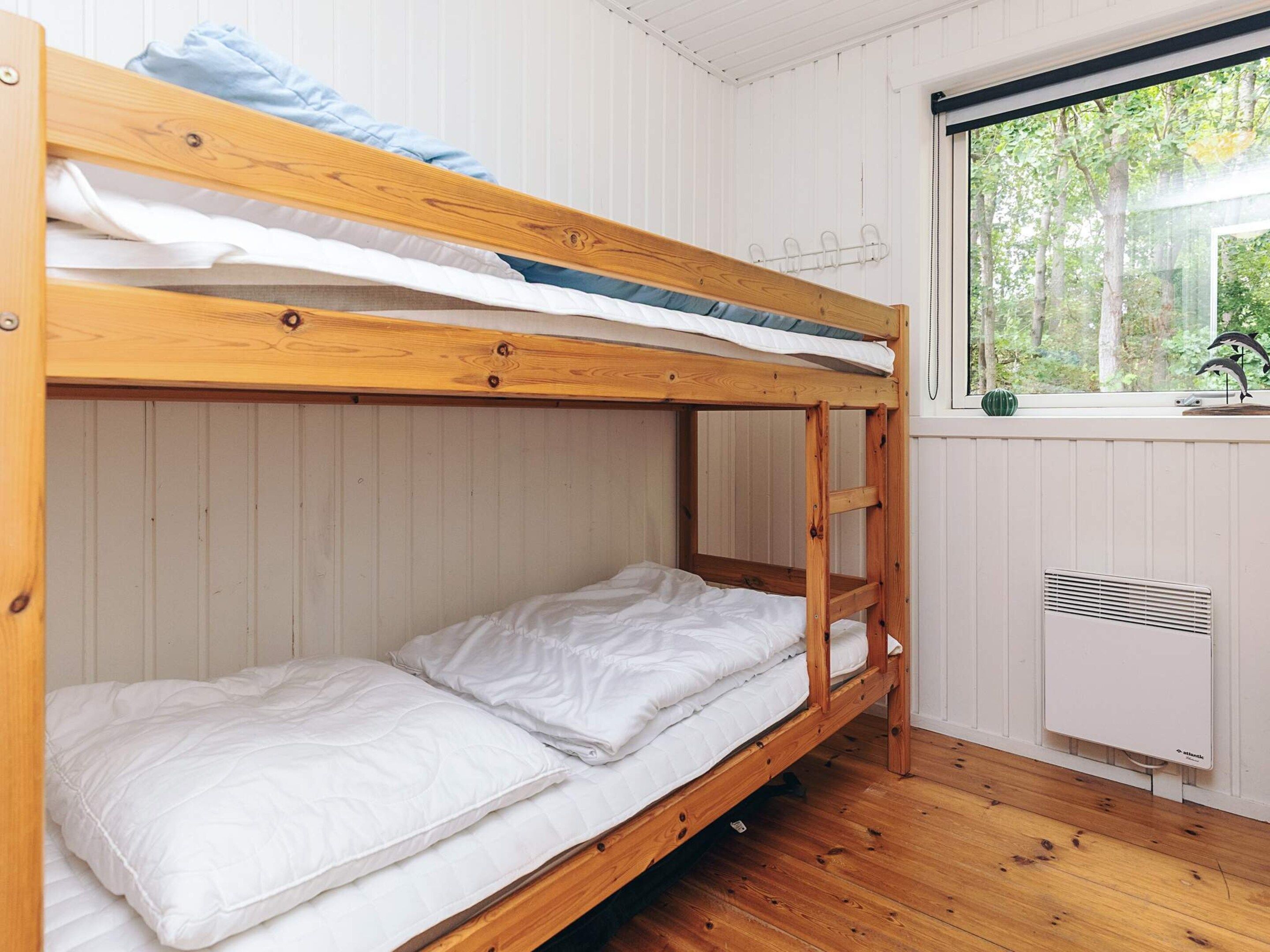 A bunk bed room with white bedding, a window with a view of trees, and a radiator.